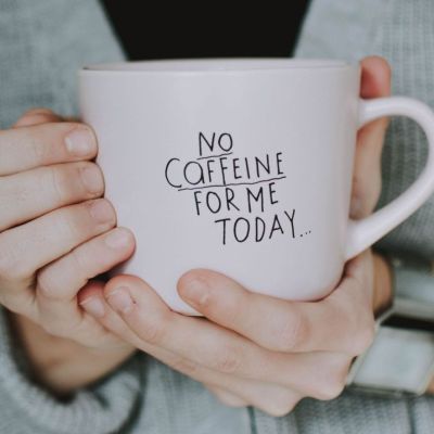 Close-up of a person in a sweater holding a mug with 'No Caffeine for Me Today' text.