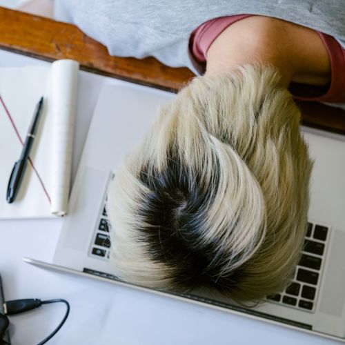 From above of tired fatigued unrecognizable female in casual wear resting head on netbook keyboard near notebook and cup of tea after long working day